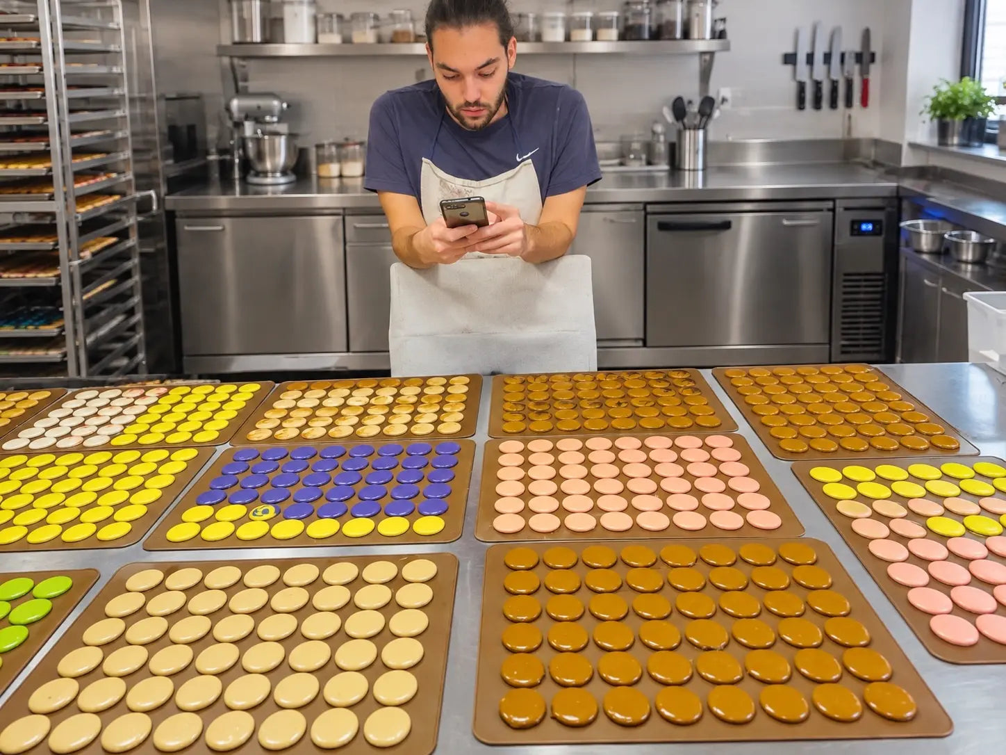 Baker standing behind trays of colourful macaron shells