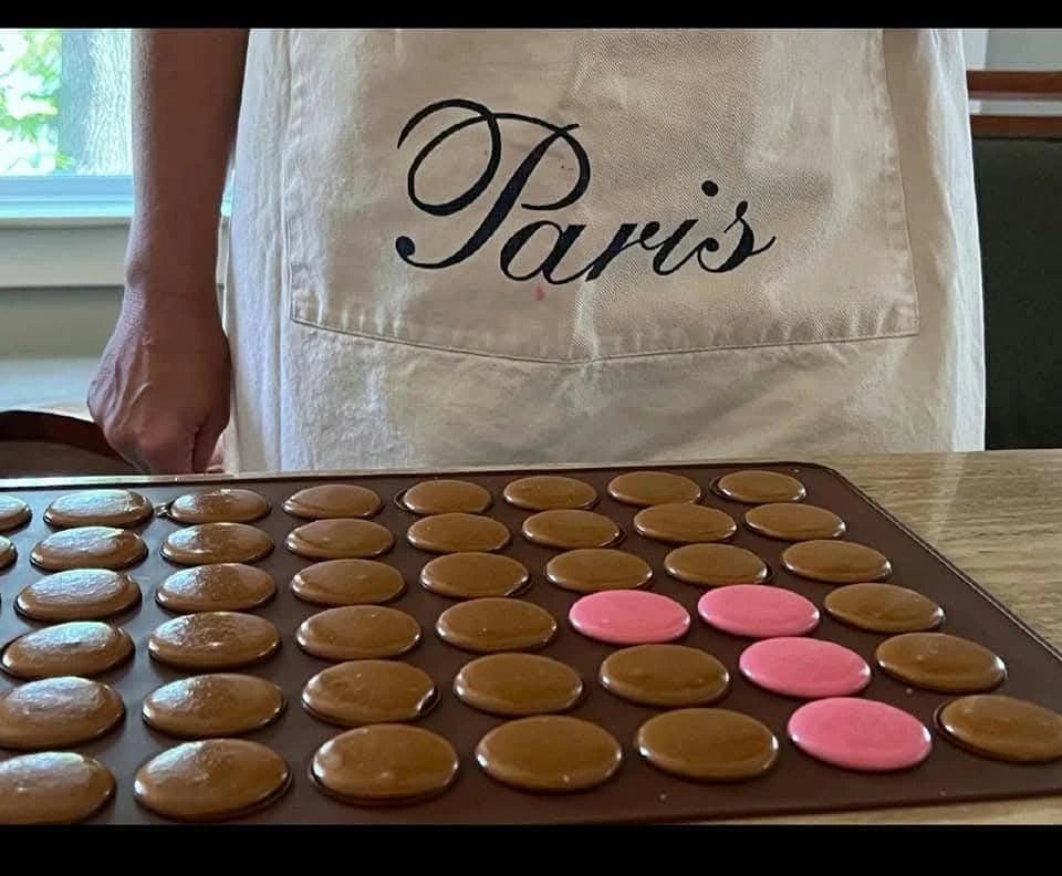 Fresh macaron shells arranged on a tray in front of a Paris apron