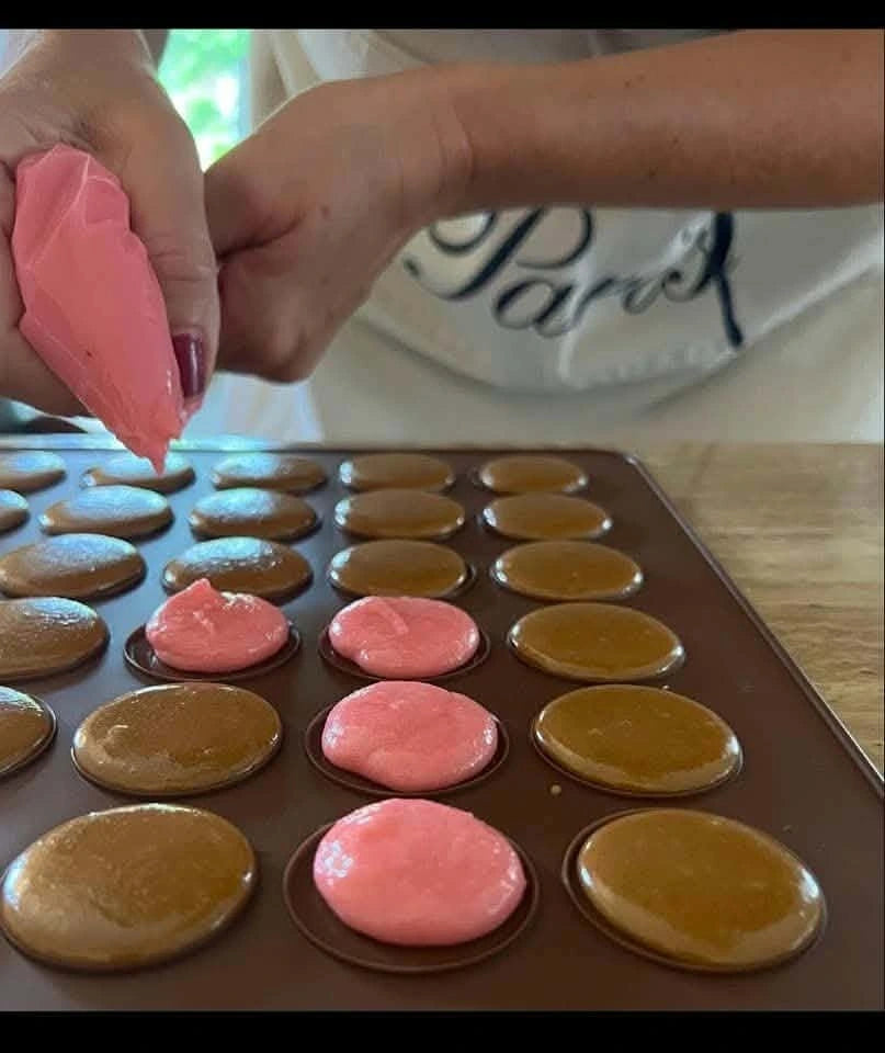 Pink macaron mixture being piped onto a baking mat